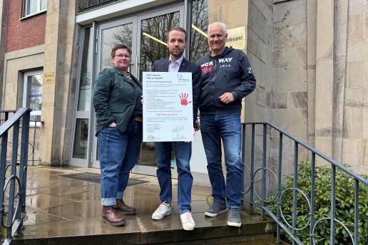 Drei Personen stehen mit einem Plakat, Aufschrift "Grundsatzerklärung gegen Gewalt", auf den Stufen vor dem Rathaus Waltrop. 