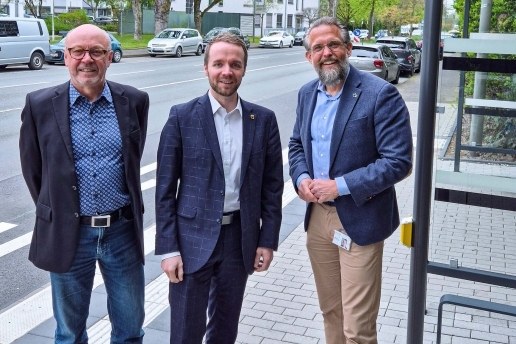 Drei Herren stehen an einer Bushaltestelle. 