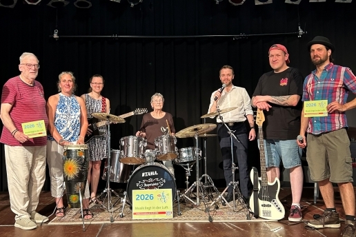 Eine Gruppe von Personen steht mit Musikinstrumenten auf einer Bühne.