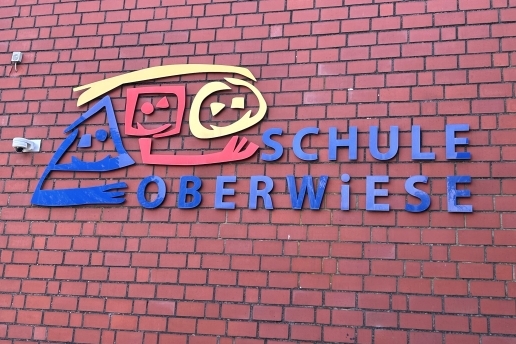Das Logo der Schule Oberwiese in Rot, Gelb und Blau an einer Klinkerfassade.