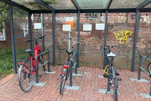 Drei Fahrräder stehen an einer überdachten Fahrradabstellanlage. 