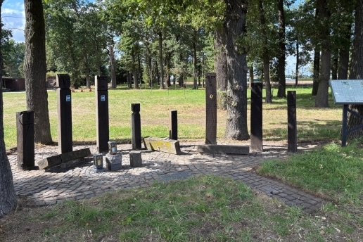 Holz-Stelen am Mahnmal Holthausen, im Hintergrund eine Grünfläche, drum herum Bäume. 