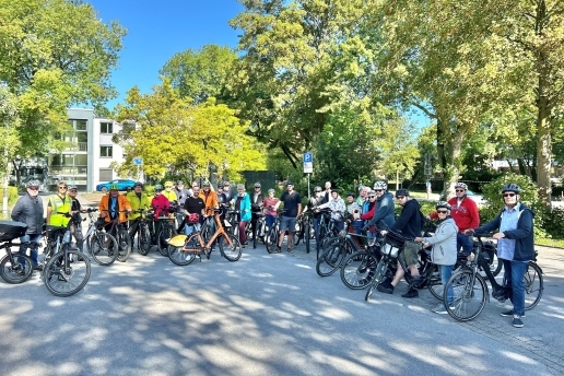Eine Gruppe steht mit Fahrrädern auf dem Parkplatz vor dem Rathaus.