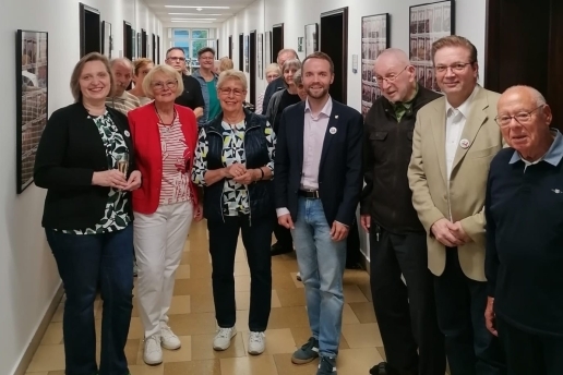 Eine Gruppe Menschen steht vor Bilderrahmen im Flur des Rathauses. 