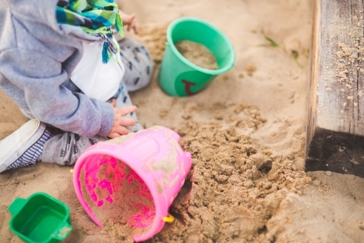 Symbolbild: Sandkasten-Spielfläche für Kinder. Auf dem Bild: Kind spielt im Sand mit Eimer und Förmchen. 