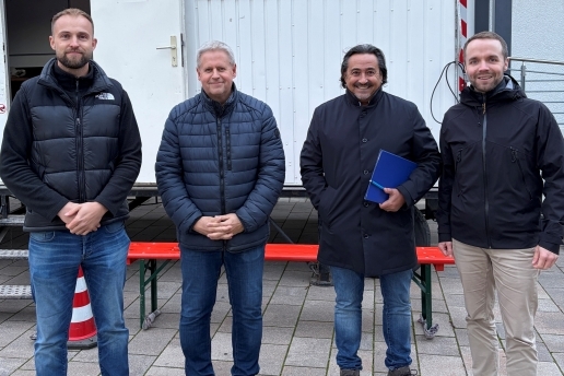 Vier Männer stehen vor einem Bauwagen.