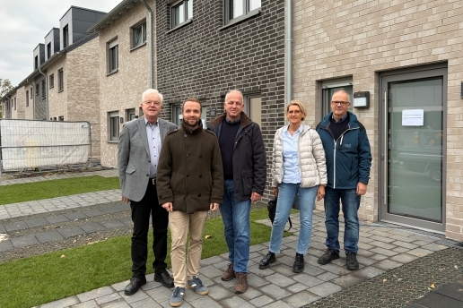 Vier Männer und eine Frau stehen vor Reihenhaus-Neubauten mit Klinkerfassade